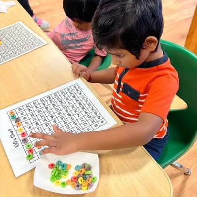 Child counting with colorful cereal pieces on a 100s chart